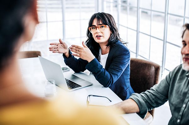 A woman sits in front of her laptop and discusses with her colleagues.