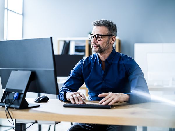 A man sits at a desk and looks at a screen.
