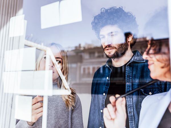 Three people are standing in front of a wall discussing notes.