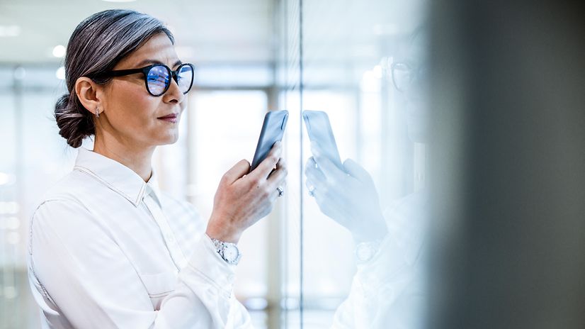 Smiling woman standing in front of an office window with a smartphone in her hand