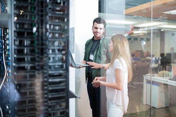 Man with laptop and woman standing in front of data centre with cloud servers.