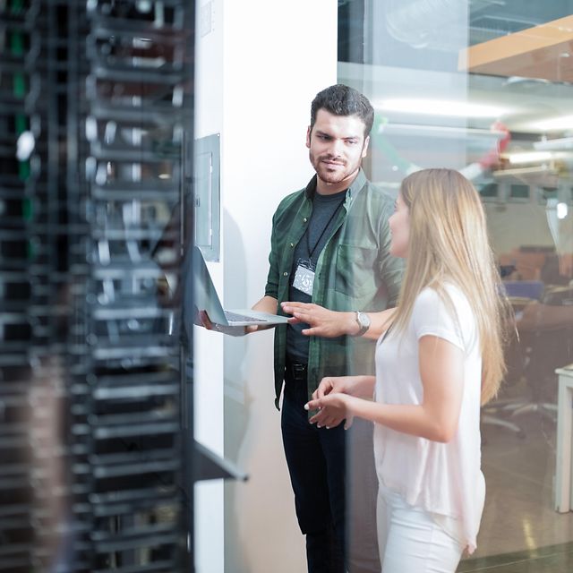 A woman and a service technician are standing in front of a server cabinet talking about Business LAN Cisco.