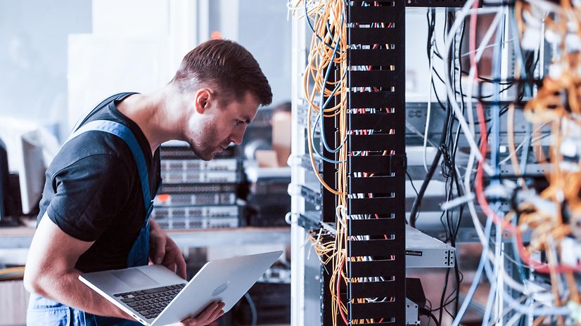 A technician with a laptop in front of a server cabinet for Secure SD-WAN – Fortinet