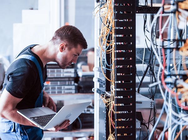 A technician with a laptop in front of a server cabinet for Telekom SD-WAN based on Fortinet