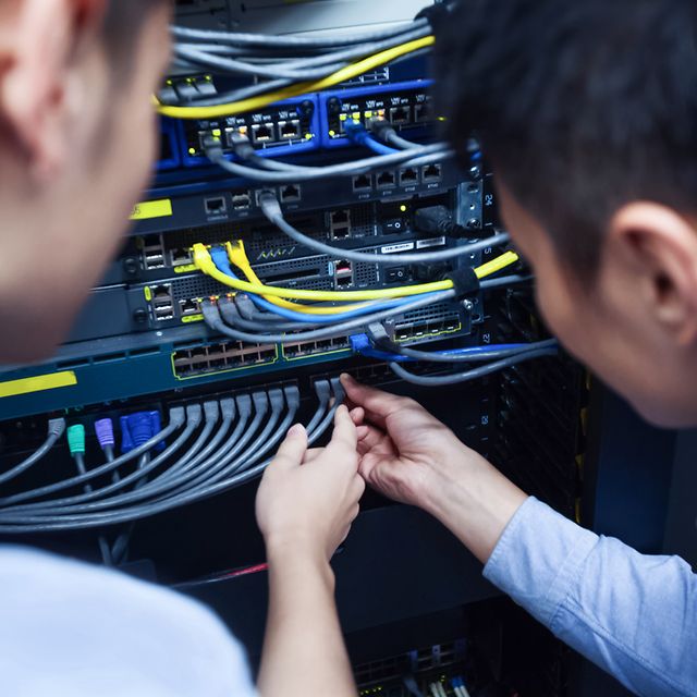 Two technicians inspect cables on a rack cabinet.