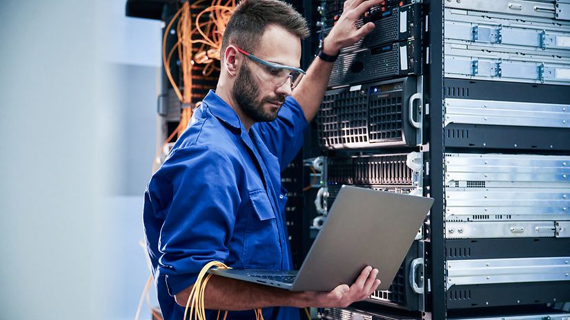 Young man with laptop working with internet devices and cables in the server room