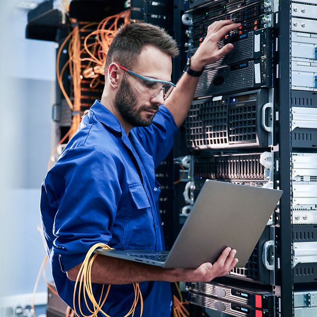 Young man with laptop working with internet devices and cables in the server room