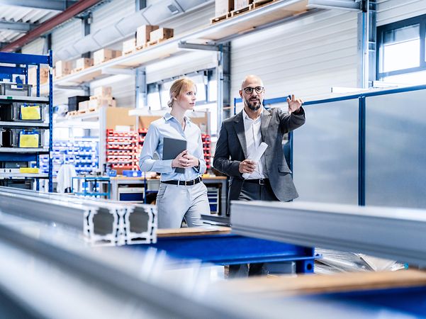 A woman and a man in business attire are discussing matters in a warehouse.