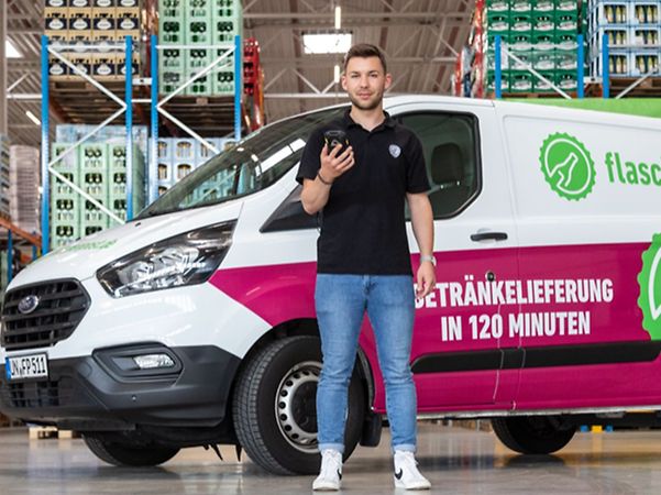 Employee with mobile phone in front of his delivery vehicle by flaschenpost