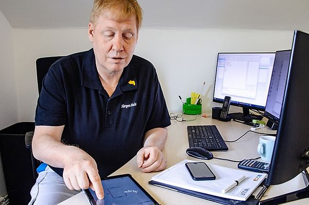 Master painter Juergen Hahn in a blue T-shirt typing on a tablet at his office desk