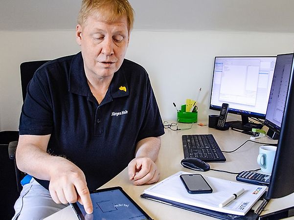 Master painter Juergen Hahn in a blue T-shirt typing on a tablet at his office desk