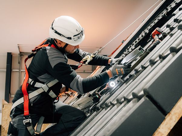 Enpal employee wearing a helmet and protective gear installs a solar power system on the roof.