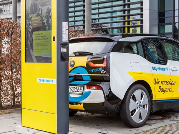 Blue and white electric vehicle at Bayernwerk's yellow charging station