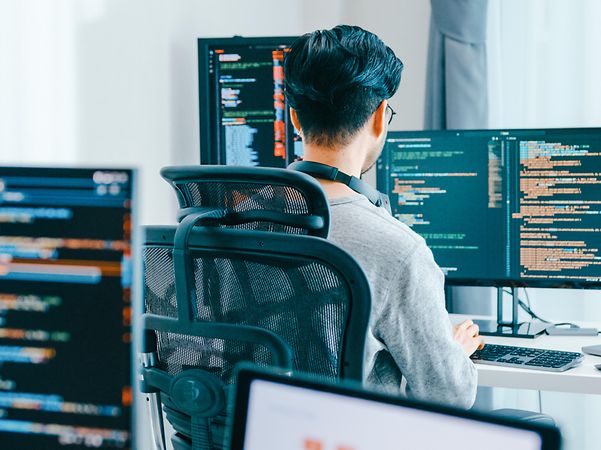 View over the shoulder of a developer at computer screens displaying lines of code.