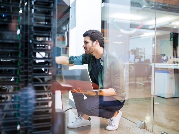 A man is making adjustments to a server in an office.