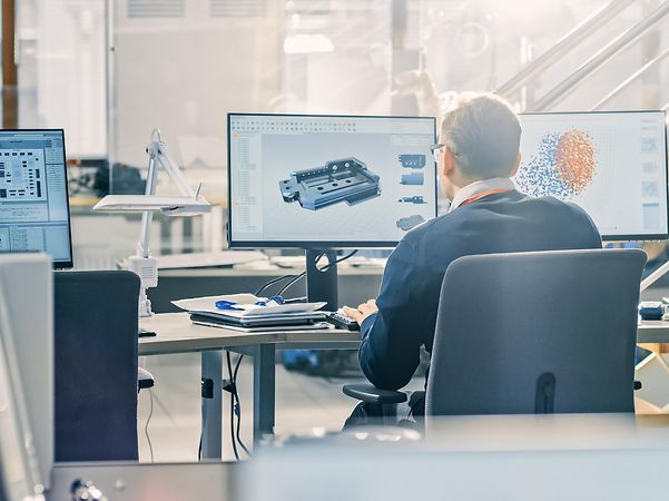 A man works at a computer with two monitors in an office.
