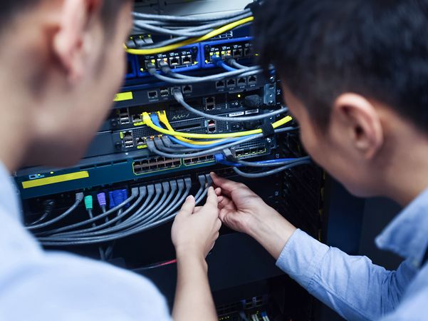 Two technicians inspect cables on a rack cabinet.