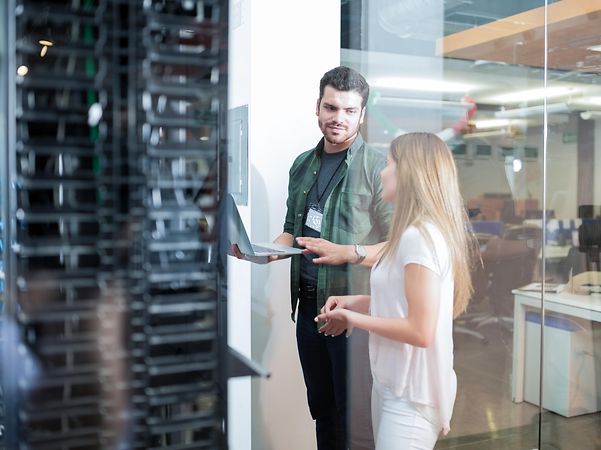 Two security experts in front of a server cabinet discuss strategic security services.