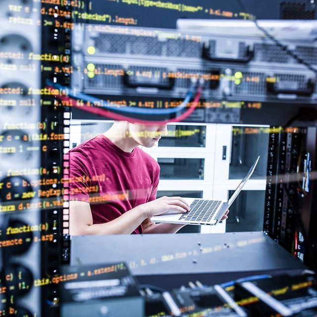 Person in the data centre working with a laptop between server cabinets, overlaid with programme code on the screen.