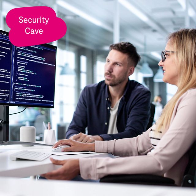 Two people are looking at source code on large monitors in a modern office and discussing it.