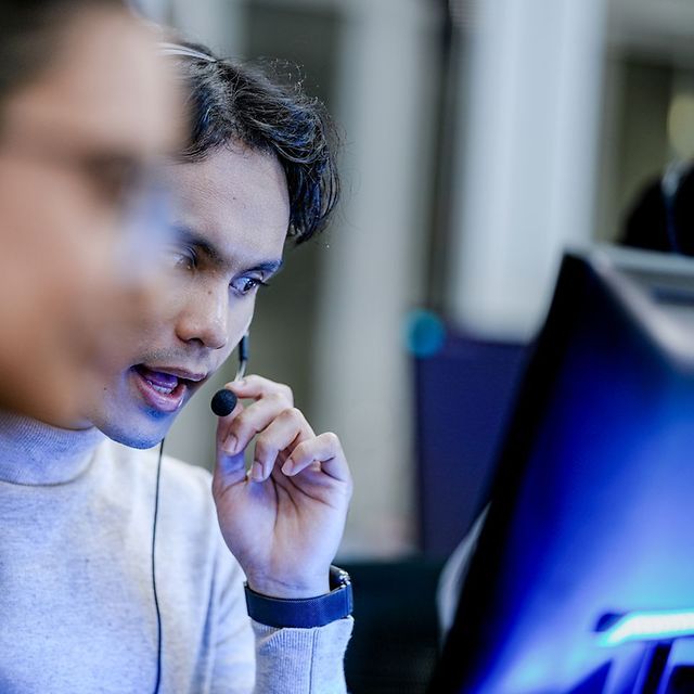 Person wearing a headset concentrates on a desktop monitor in an office environment.
