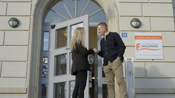 Authorised signatory Renken and account manager Schmitt shake hands in front of the entrance to the Waldpark retirement home.