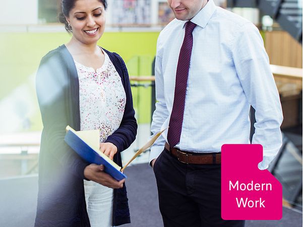 Two employees are standing in a modern office area, chatting.