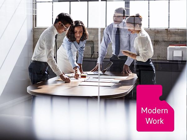 Arbeitsgruppe im modernen Büro steht um einen Tisch und bespricht Unterlagen, durch Glaswand fotografiert