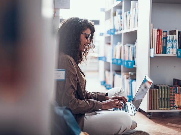 A woman is sitting in a library, looking up information about Security OnNet Comfort