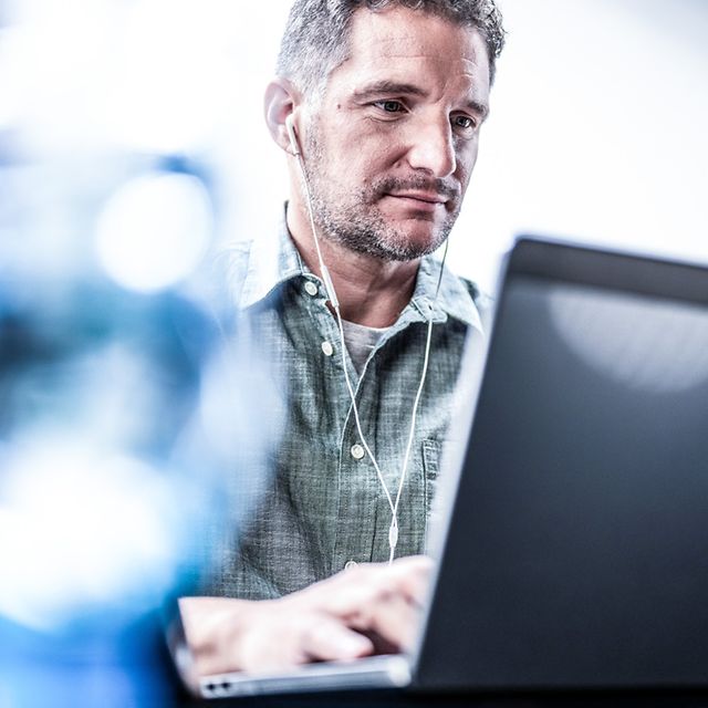 Mann mit Kopfhörern tippt konzentriert am Laptop, davor unscharfe blaue Lichtreflexionen (Bokeh).