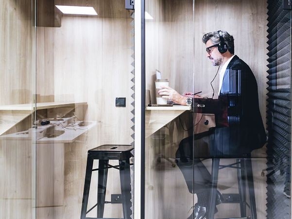 An executive who is engrossed in their work is wearing headphones in a soundproof booth
