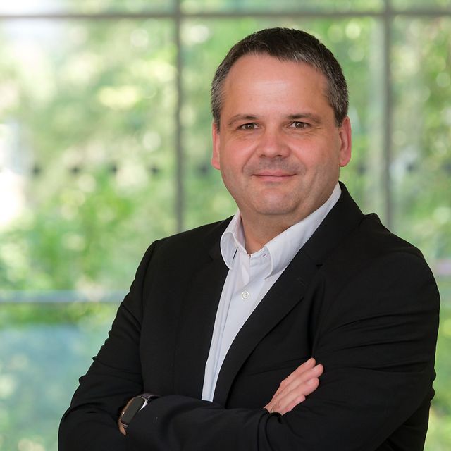 Portraitfoto von Thomas Tschersich von Telekom Security in weißem Hemd und schwarzem Blazer vor grünem Hintergrund