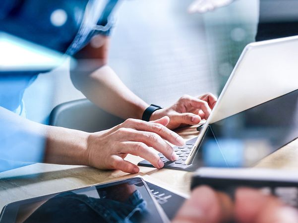 Team arbeitet gemeinsam an Laptops, Tablet und Smartphone auf einem Schreibtisch mit digitaler Netzwerk-Überblendung.