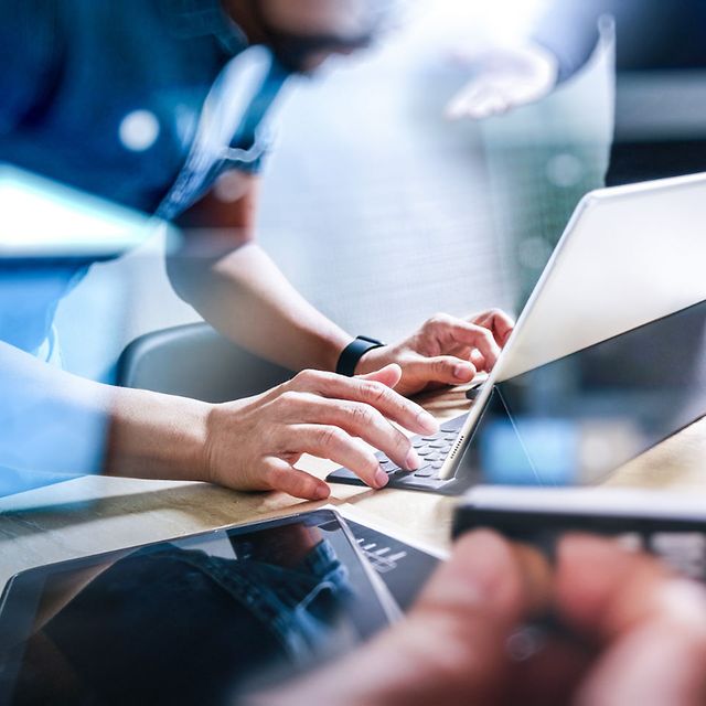 A team works together on laptops, tablets and smartphones on a desk featuring a digital network overlay.