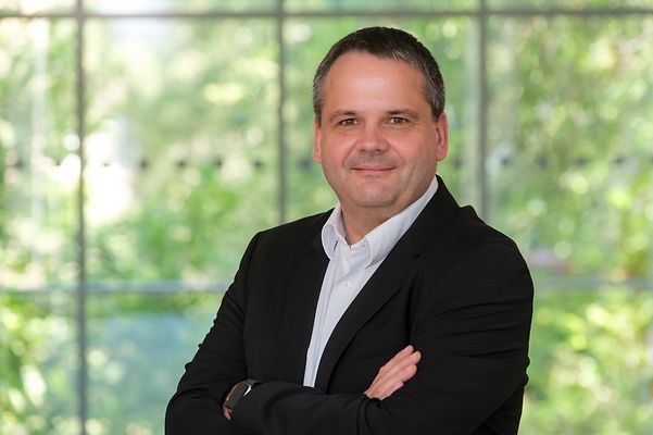 Portraitfoto von Thomas Tschersich von Telekom Security in weißem Hemd und schwarzem Blazer vor grünem Hintergrund