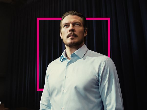 Trust-the-T CEO im blauen Hemd schaut ueberlegt und forsch mit Magenta Grafik