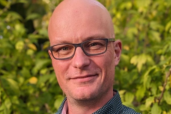 Portrait of Dominik Scherer against a green natural backdrop