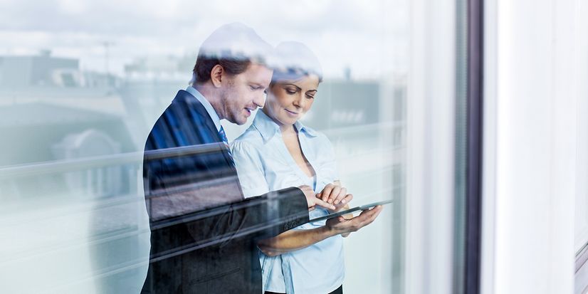 Zwei Erwachsene im Business Outfit betrachten den Telekom Festnetz Tarifberater und die Produktempfehlungen auf einem Tablet.