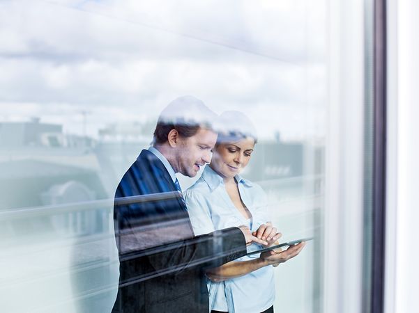 Zwei Erwachsene im Business Outfit betrachten den Telekom Festnetz Tarifberater und die Produktempfehlungen auf einem Tablet.