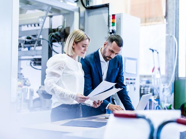Zwei Personen an einem Tisch in einer industriellen Umgebung in produktiver Teamarbeit, unterstützt durch Kollaborationstools