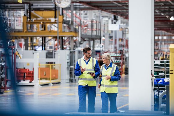 Zwei Arbeiter laufen durch eine Produktionshalle, in der 5G-Campuns Netze zu Datenübertragungen genutzt werden