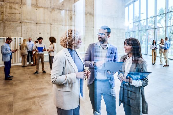 Viele Menschen in Business-Kleidung stehen in einem Foyer und reden miteinander. Sie haben teilweise Laptops und Tablets dabei.