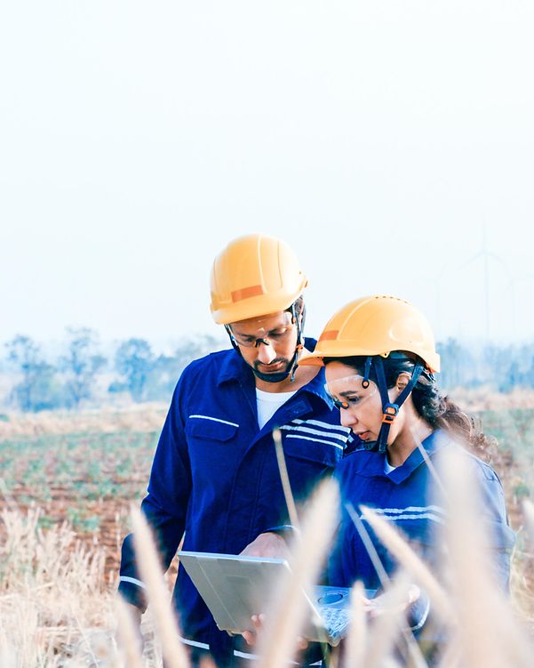 Zwei Techniker auf einem Feld nutzen Salesforce Energy & Utilities Cloud am Laptop, im Hintergrund Windräder