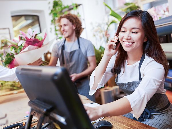 Eine junge Frau und ein junger Mann bedienen Kunden in einem Blumenladen mit digitaler Kasse