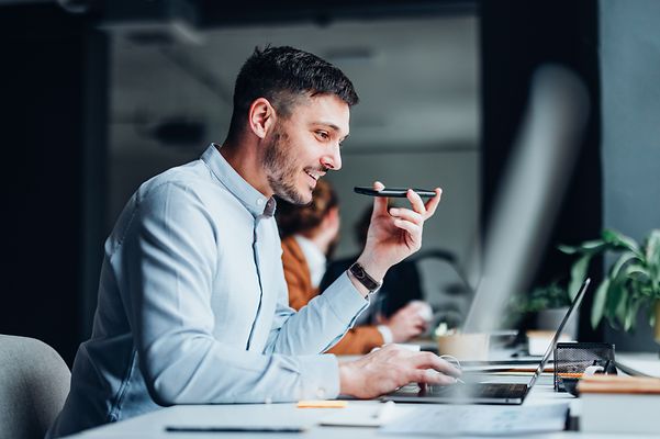 Ein Mann telefoniert mit seinem Smartphone und schaut seinen Laptop