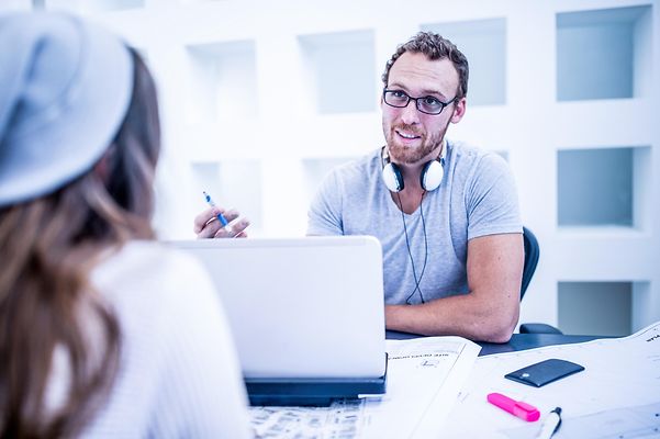 Ein Mann redet freundlich lächelnd mit einer Kollegin, Blick über die Schulter der Kollegin