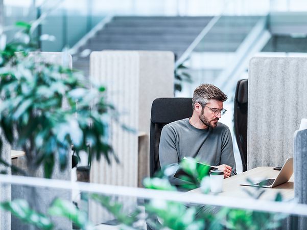 Mann sitzt in einer mobilen Arbeitsumgebung und arbeitet mit einem Laptop.
