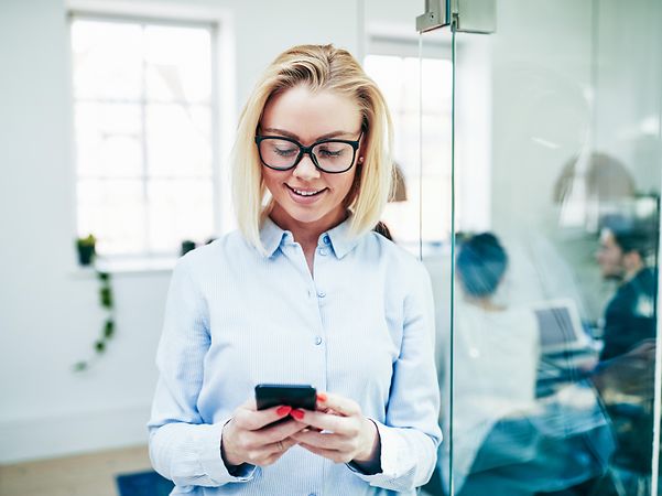 Frau liest auf Ihrem Smartphone eine SMS und lächelt