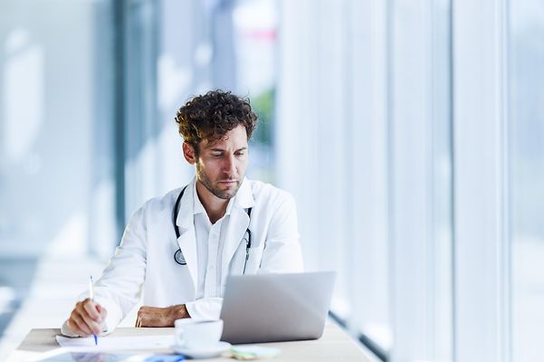 Arzt sitzt vor seinem Laptop in der Praxis und nutzt die Komponenten der Fachanwednungen für Praxen der Telekom