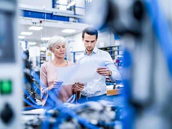 Geschäftsfrau und Geschäftsmann schauen sich den Plan in einer Fabrik an